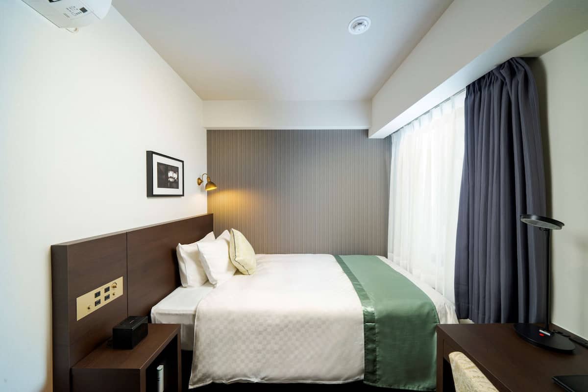 Ein Hotelzimmer mit Bett, Nachttisch, Lampe und einem an der Wand hängenden Bild.