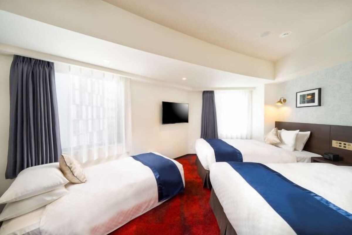 Ett hotellrum med två sängar, en röd matta, en platt-TV och ett stort fönster med gardiner.