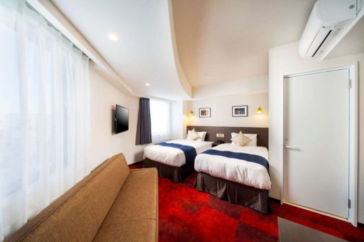 Una habitación de hotel con dos camas, un sofá, un televisor y un aire acondicionado.