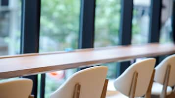 A row of chairs with wooden legs and a wooden table in front of a window with a view of trees.