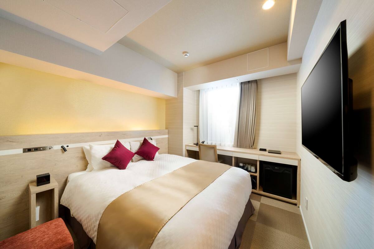 Een hotelkamer met een groot bed, een bureau, een flatscreen televisie en een raam met gordijnen.