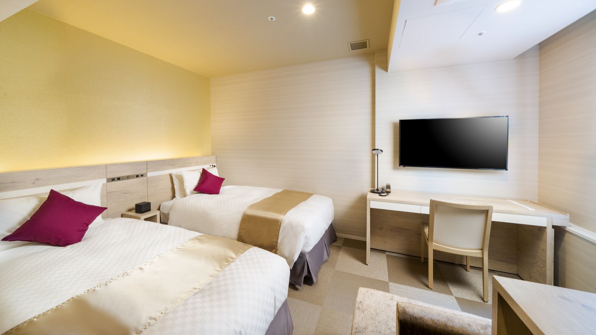A hotel room with two beds, a desk, a chair, a TV, and a small table.