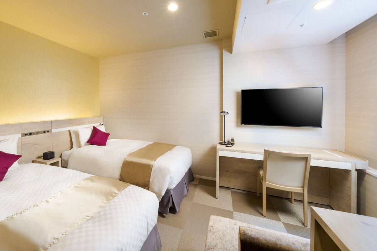 Een hotelkamer met twee bedden, een bureau, een stoel, een televisie en een klein tafeltje.