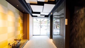Een moderne hotelentree met een geruit patroon op de muur, een houten bank met een decoratieve schaal, en een glazen deur die naar buiten leidt.