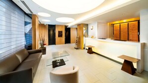 Een moderne lobby met een receptiebalie, een zithoek en een groot raam met zonwering.