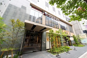 Un edificio moderno con entrada de vidrio, señalización que indica "Best Western Tokyo Akasaka" y un pequeño jardín exterior con plantas y un letrero que dice "Sushi".