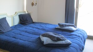 Ein Bett mit blauer Bettdecke und Kissen, eine Wandklimaanlage und ein Fenster mit Vorhang.