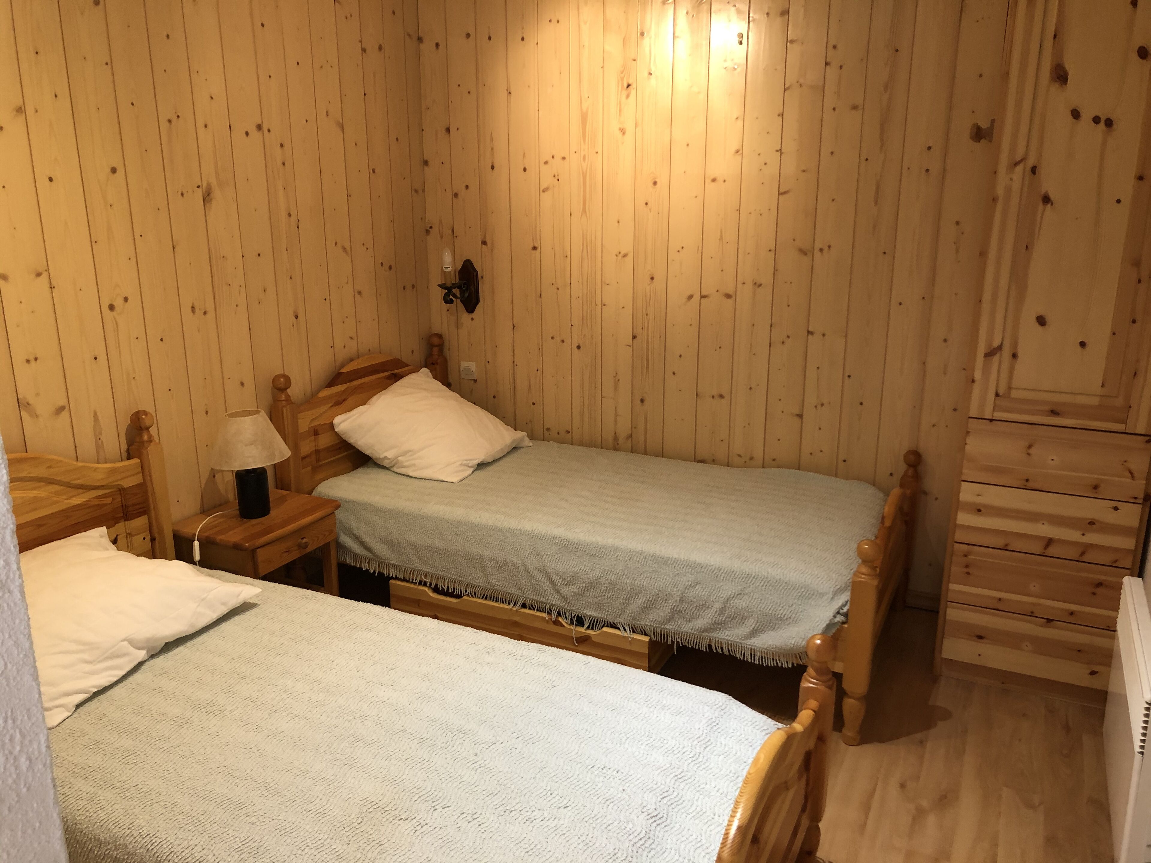 Una habitación con paneles de madera, dos camas individuales, una mesita de noche con lámpara y un aparador.