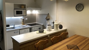 Una cocina compacta con microondas, estufa, pileta y un reloj en la pared.