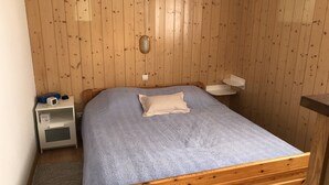 Una habitación con paneles de madera, una cama individual, una mesita de noche, un pequeño estante y una lámpara fijada a la pared.