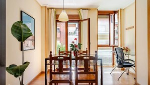 A dining area with a wooden table and chairs, a potted plant, and a view of the street outside. - Natural light, quiet, and in a great location (Madrid)