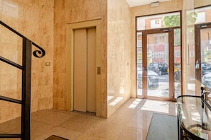 A hotel lobby with a marble floor, a closed elevator, and a glass door leading outside.