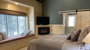 Ein gemütliches Schlafzimmer mit einem großen Bett, einem Kamin, einem Fernseher und einer Sitzbank an einem Fenster.