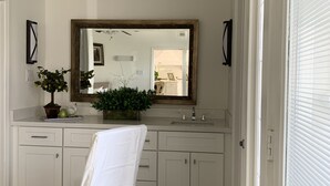 Ein modernes Badezimmer mit großem Spiegel, weißen Schränken und einer Zimmerpflanze.