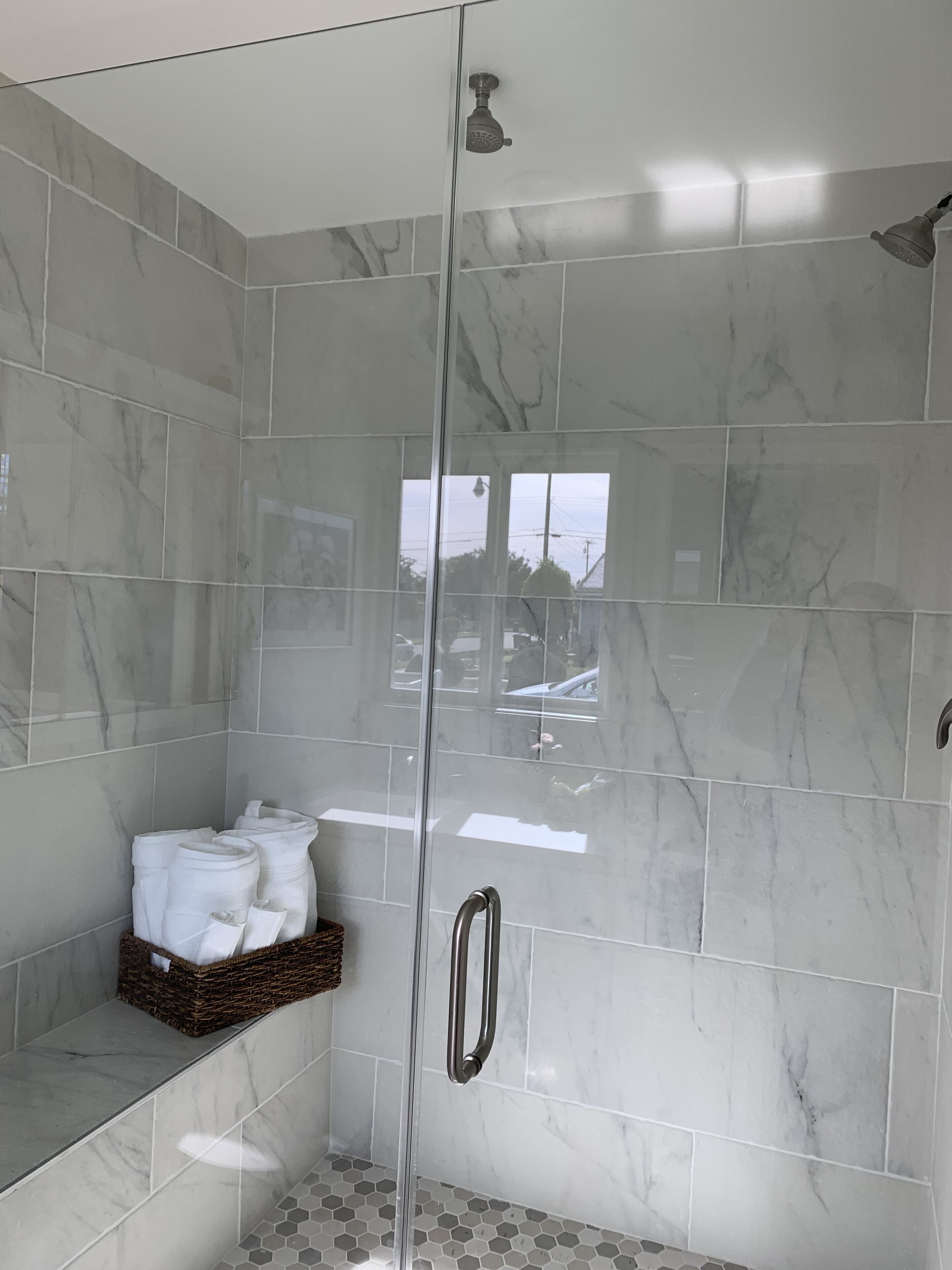 Um chuveiro de acesso livre com azulejos de mármore, porta de vidro e puxador de metal.