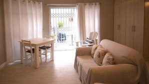 A room with a wooden dining table and chairs, a beige sofa, and a wardrobe. - Apartment Melkbos Moments-Apartment with a Pool View (Melkbosstrand)
