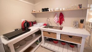 A compact kitchen with white cabinetry, a built-in sink, and a red kettle. - Apartment Melkbos Moments-Apartment with a Pool View (Melkbosstrand)