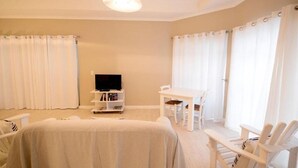 A room with a bed, a TV on a stand, a small table, and two chairs. - Apartment Melkbos Moments-Apartment with a Pool View (Melkbosstrand)