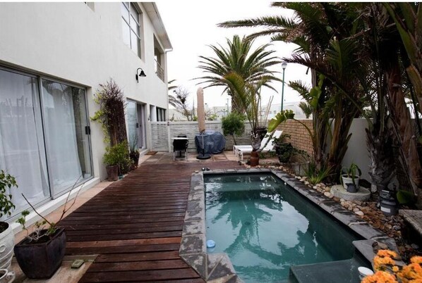 A pool area with a wooden deck, surrounded by potted plants and palm trees.