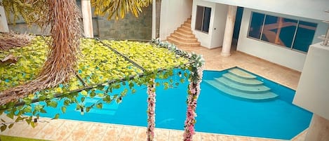 A modern indoor pool area with a clear blue pool, surrounded by a tiled floor and a green artificial grass area.