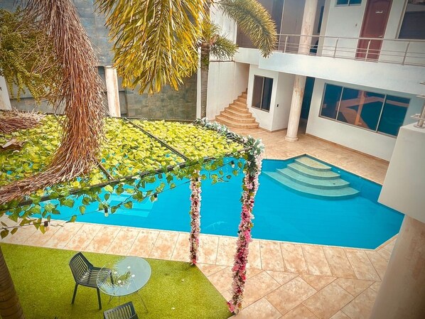 A modern indoor pool area with a clear blue pool, surrounded by a tiled floor and a green artificial grass area.