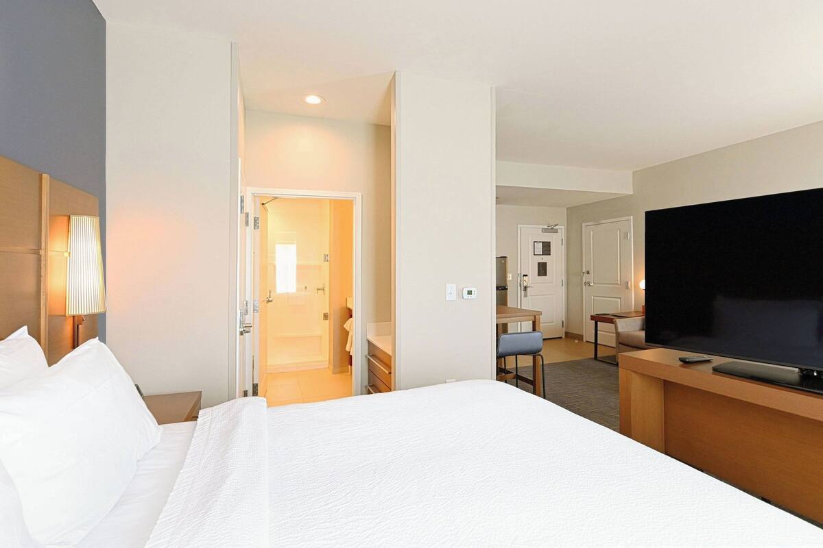 A hotel room with a large bed, a TV, a desk, and a chair.