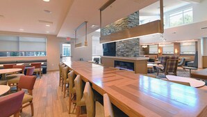 A modern restaurant with a long wooden bar, cushioned seating, and a stone accent wall. - Residence Inn by Marriott Richmond West/Midlothian (Richmond)
