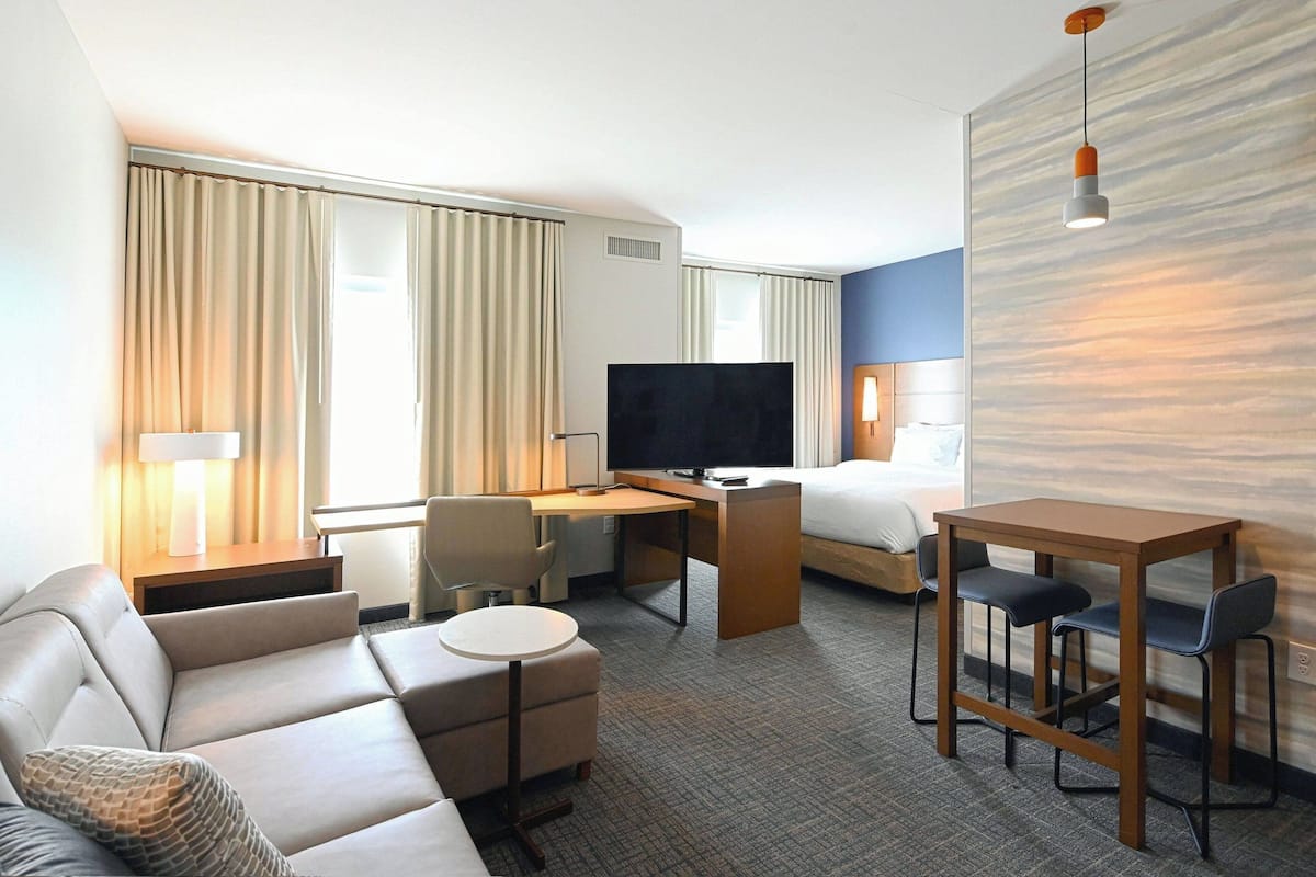 A hotel room with a sofa, a desk, a TV, a bed, and a small table with chairs.