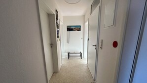 Un pasillo estrecho con paredes blancas, alfombra de color claro y un banco al final.