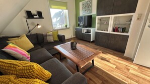 Una sala de estar moderna con un sofá modular gris, una mesa de centro de madera y un televisor sobre un mueble bajo.