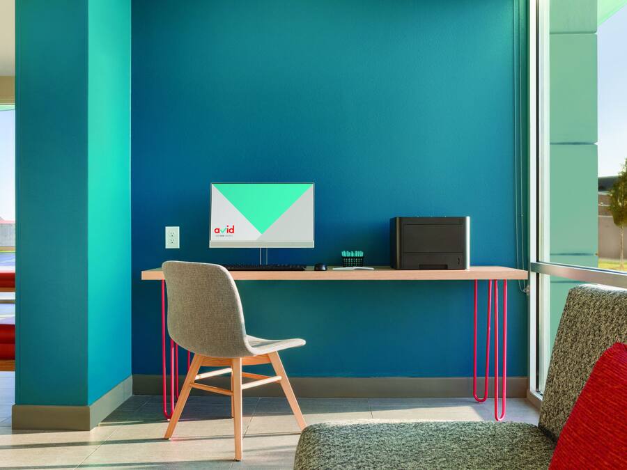 Um espaço de escritório moderno com parede verde-água, uma mesa com um computador, uma cadeira e um sofá com uma almofada vermelha.