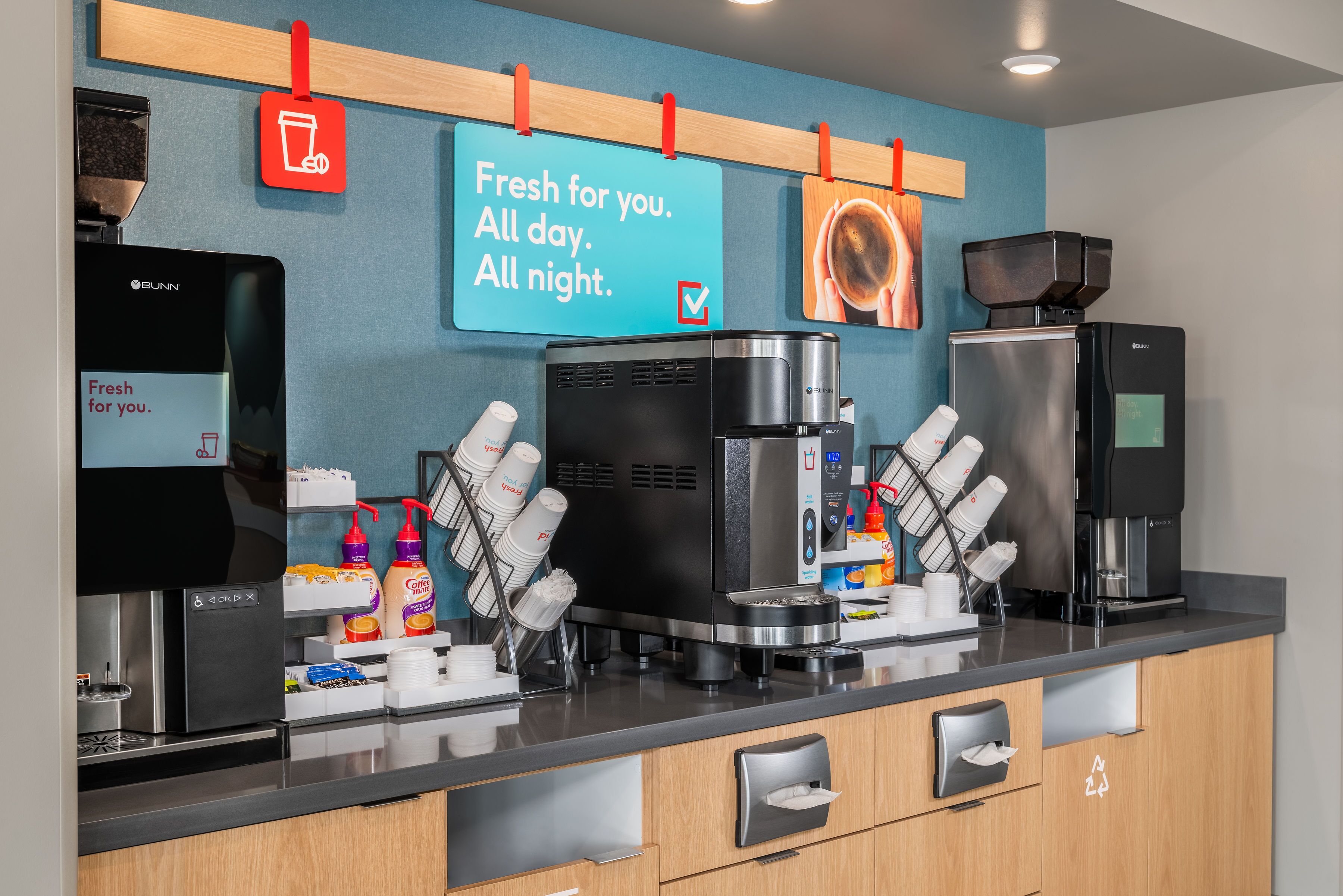 A coffee station with multiple coffee machines, a coffee grinder, and a sign that reads "Fresh for you. All day. All night."