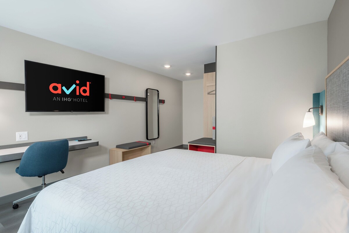 Una habitación de hotel moderna con cama, escritorio, silla, televisor y espejo.