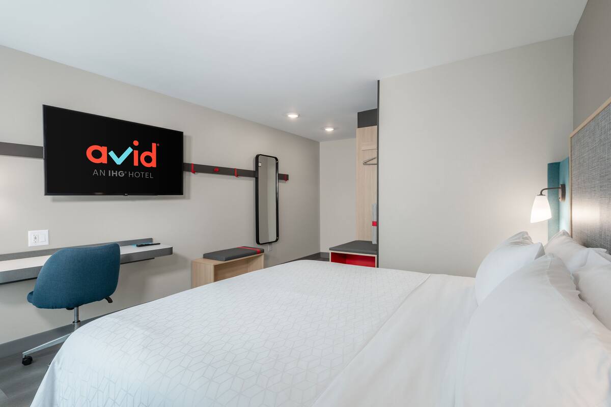 Een moderne hotelkamer met een bed, een bureau, een stoel, een televisie en een spiegel.