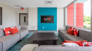 Un hall d’hôtel moderne avec des canapés gris, une table basse noire et une grande fenêtre donnant sur un mur rouge à l’extérieur.