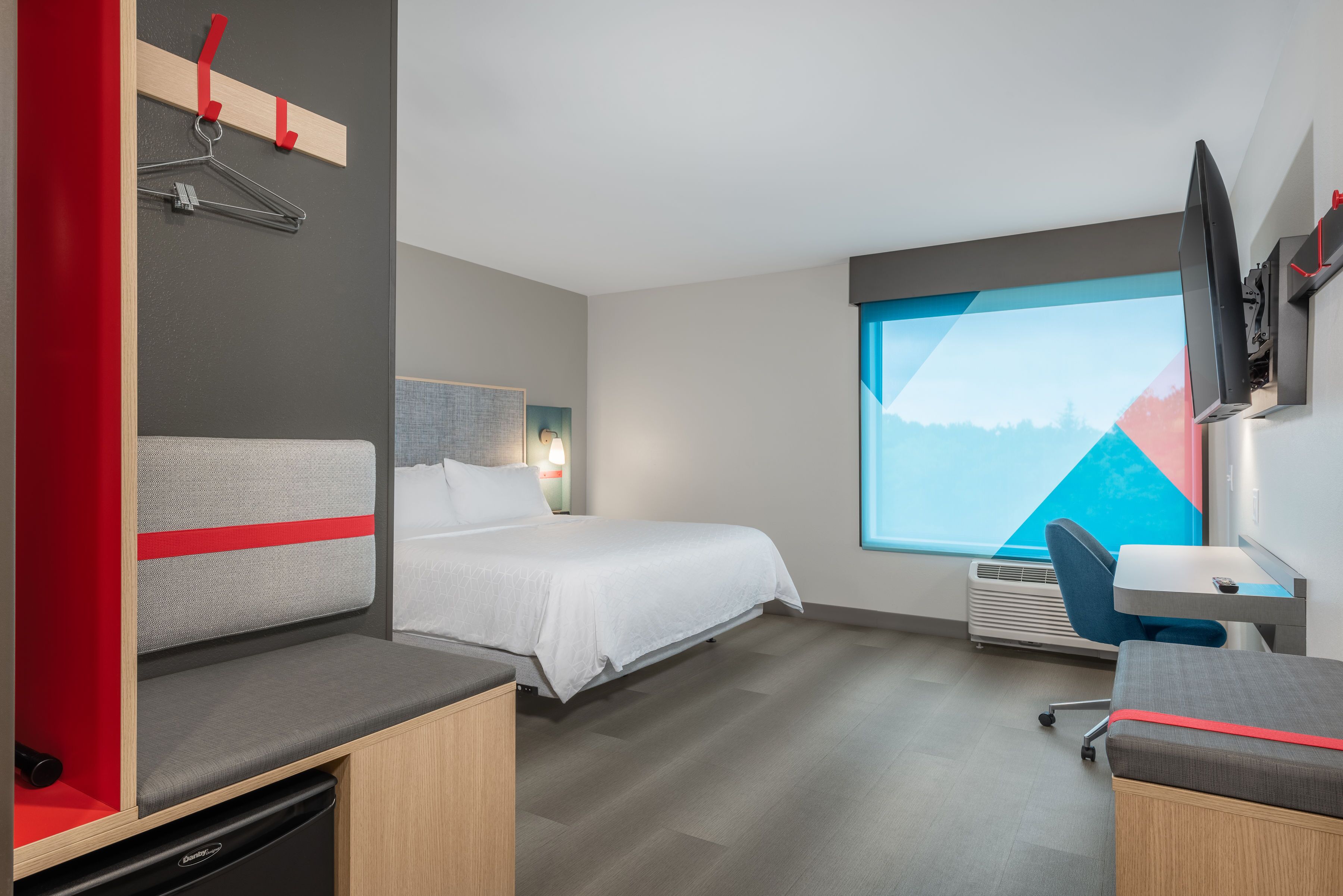 A modern hotel room with a bed, a desk, a chair, a TV, and a window with a mountain view.