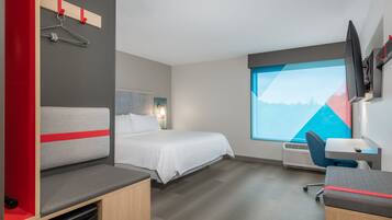 A modern hotel room with a bed, a desk, a chair, a TV, and a window with a mountain view.