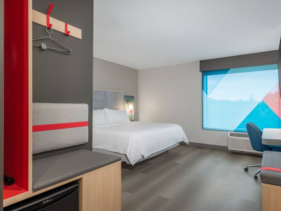 A modern hotel room with a bed, a desk, a chair, a TV, and a window with a mountain view.