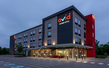 A modern hotel building with a prominent 'avid' sign, multiple floors, and a parking lot with handicapped spaces.