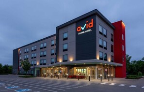 Ein modernes Hotelgebäude mit einem gut sichtbaren 'avid'-Schild, mehreren Etagen und einem Parkplatz mit Behindertenparkplätzen.