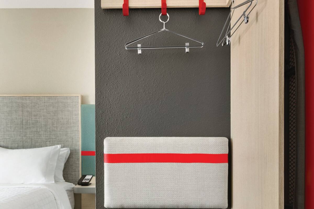 Een compacte hotelkamer met een bed, een klein bureau, een nachtkastje, een ingebouwde televisie en een minibar.