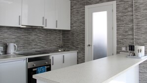 A modern kitchen with white cabinets, a stainless steel sink, and a grey tiled backsplash.