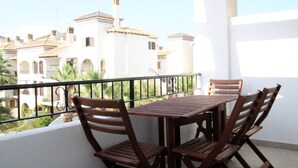 A balcony with a wooden table and chairs, overlooking a residential area with white buildings and palm trees.