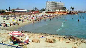 A beach with a hotel in the background, sandy beach, and people swimming.