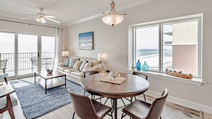 A spacious living room with a round dining table, a sofa, and a balcony with a view of the ocean.