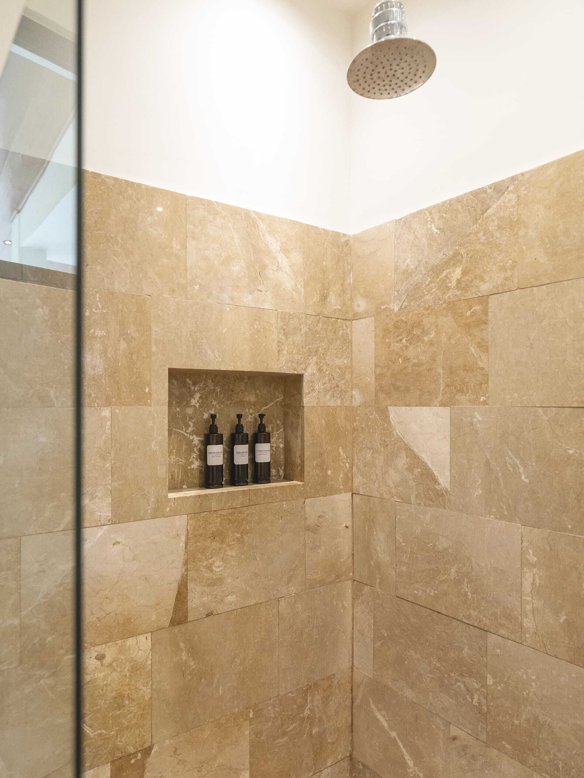 A shower room with beige tiles and a shelf holding three bottles.