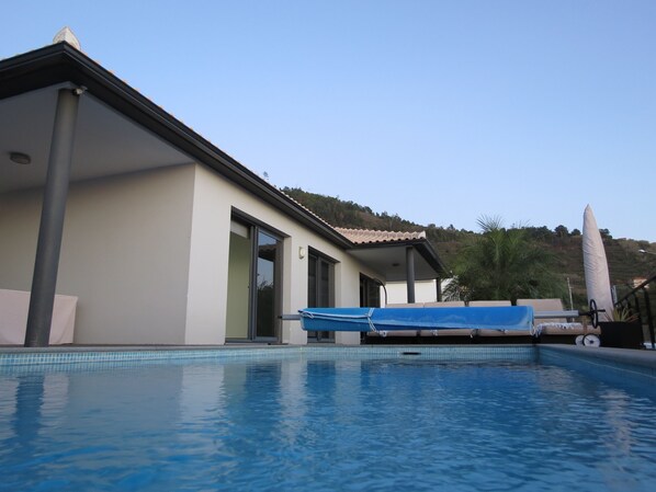 Une maison moderne dotée d’une piscine, de grandes fenêtres et offrant une vue sur une colline.