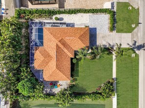 Luchtbeeld van een gebouw met een opvallende geometrische dakconstructie, omgeven door weelderige begroeiing en een verzorgd gazon.