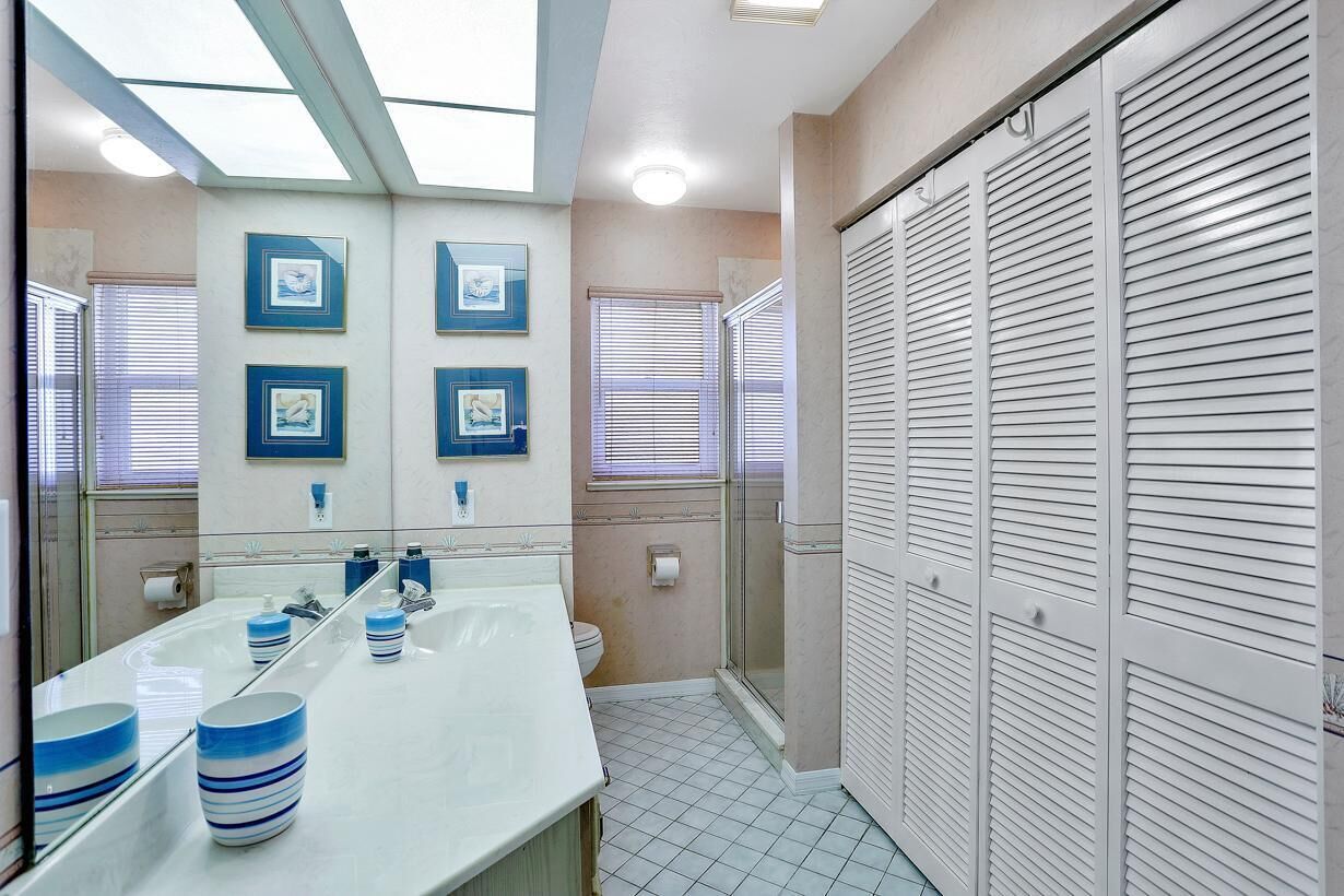 A bathroom with a large mirror, a sink with blue-striped soap dishes, and a walk-in shower.