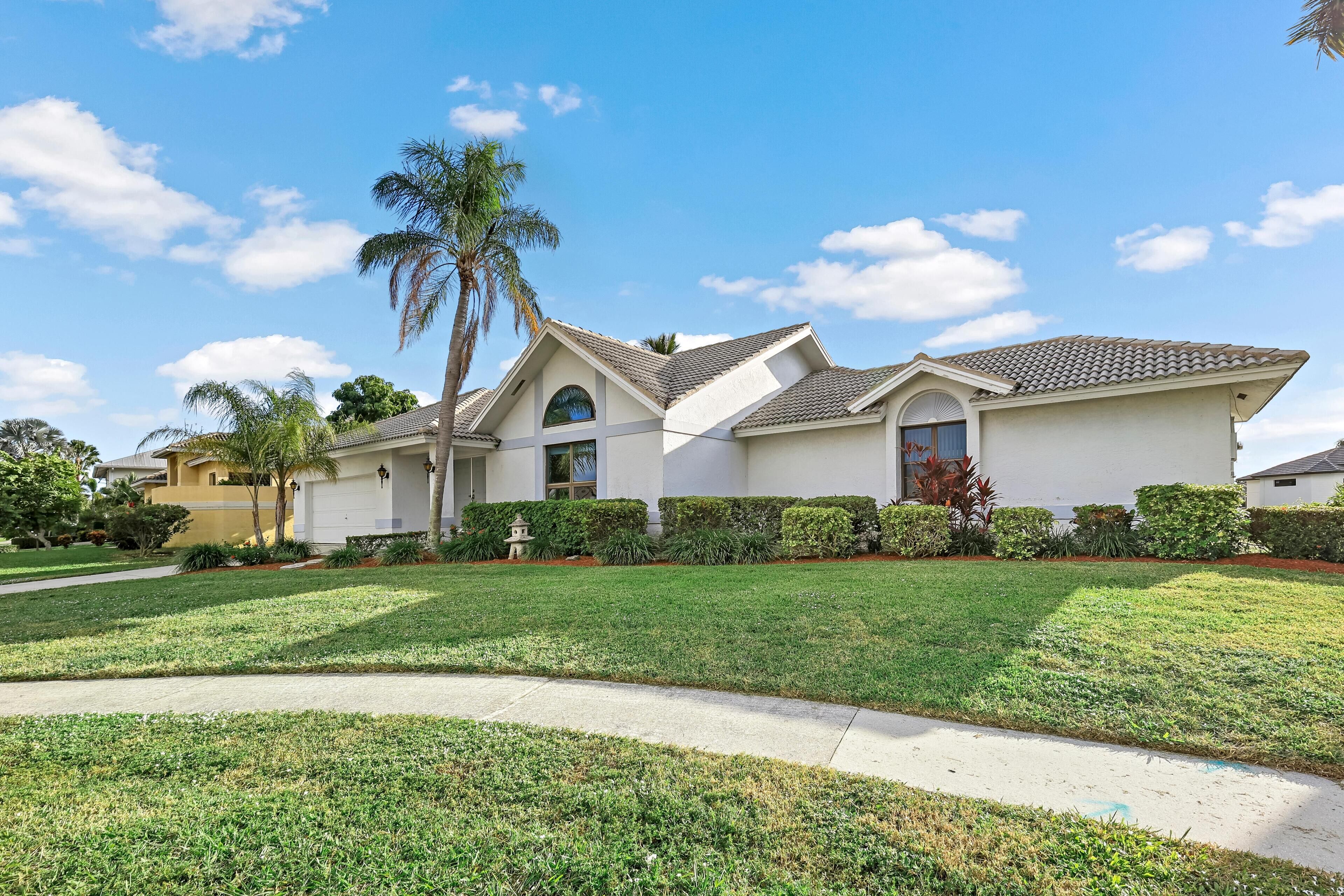 A modern two-story house with a well-maintained lawn, a driveway, and a palm tree.